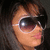 Pixelated close-up of a person's face with dark hair, wearing large reflective sunglasses against a dark background.