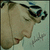 Pixelated image of a person in profile wearing dark goggles and light clothing against a pale background with faint abstract shapes.