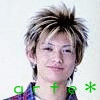 A person with spiky blonde and brown hair wears a blue and red plaid shirt against a white background, with green and blue text below the neck.