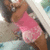 A pixelated image shows a person with brown skin wearing a pink sleeveless top and dark shorts, holding an object near their face.