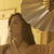 A pixelated image shows a person with long dark hair in a dimly lit room with warm yellow tones and a white vertical element on the left.