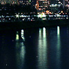 Dark water surface reflecting vertical light streaks from a distant illuminated structure above.