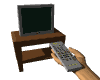 A hand holds a gray remote control aimed at a dark television on a wooden stand, with the TV screen displaying various static and animated patterns