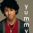 Pixelated image of a person with dark curly hair wearing a red sleeveless top over a dark long-sleeve shirt and a necklace, with vertical white text reading YUMMY on the right.