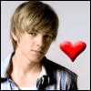 A person with light brown hair in a blue and white striped shirt stands against a light gray background with a red heart icon to the right.