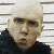 Pixelated portrait of a person with light-colored hair wearing dark clothing against a striped background.