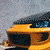 A yellow sports car with black accents and silver alloy wheels is shown in two overlapping views, one angled front-left and the other side-rear.