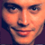 Pixelated close-up of a smiling person's face with warm orange and brown tones, dark eyebrows, and visible teeth.