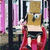 Pixelated static image shows a figure in red dress holding a golden box with green emblem, standing before pink and black vertical structures.