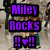 Pixelated image of a woman with long brown hair in motion, wearing white top and teal pants, with purple text reading "Miley Rocks !!❤!!" on left side.