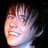Pixelated close-up of a person's face with closed eyes, smiling mouth, and reddish-brown hair against a dark background.