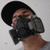 A person wearing a black cap and dark gray respirator mask against a light gray background, with two distinct facial expressions shown in sequence.