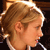 Pixelated close-up of a person's head in profile view with light brown hair tied up, showing ear and side of face against dark background.