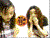 Two women in white shirts interact with a circular orange object; one woman covers her face while the other looks down.