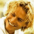 Pixelated static image of a smiling person with light brown hair and dark eyes, wearing a white shirt against a yellowish background.