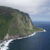Pixelated coastal landscape with green terrain, rocky cliffs, and blue water under a light sky.
