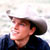 Pixelated static image of a person wearing a dark cowboy hat and dark jacket against a light background, with visible dithering and compression artifacts.