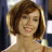 A pixelated close-up of a person with short brown hair, light skin, and a smiling expression, wearing a light-colored top against a blurred background.