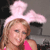 A person with light brown hair wears a large pink bunny ear headband and a bright pink sleeveless top against a dark background.