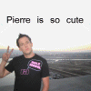 A person in a black t-shirt with a speech bubble logo makes a peace sign against a blurred landscape background, with text reading "Pierre is so cute" above.