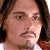 Static pixelated image of a person with long dark hair, light skin, and a mustache, wearing a white shirt with a dark collar.