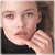 A static pixelated image shows a person with light skin, dark hair tied back, wearing a black top, and holding a hand near their face.