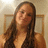 A pixelated static image shows a person with long brown hair wearing a dark top, seated against a light-colored wall with wooden trim.