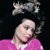 Pixelated image of a person with light skin wearing a pink top and a dark necklace, with a large bow above their head against a black background.
