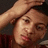 Pixelated close-up of a person with light skin tone, dark hair, and a hand raised near the forehead against a dark background.