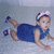 A child in a blue dress and pink headband lies prone on a light surface, with one arm extended forward.