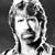 Black-and-white pixelated static image of a person's face with visible hair and facial features rendered in grayscale tones on a dark background.