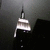 A dark, pixelated image of a building with a spire and striped facade, partially obscured by darkness and a light gray overlay.