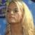 Pixelated close-up of a person with long blonde hair, light skin, and dark eyes, wearing a dark necklace against a blue and green background.