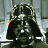 Darth Vader in a metallic suit with striped chest plate, black cape, and helmet, seated against a gray industrial background.