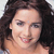 A pixelated close-up of a person with dark curly hair, light skin, and a slight smile, wearing a strapless top against a light background.
