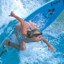 A pixelated figure in a bikini swimsuit performs a dynamic pose with arms and legs extended against a blue water background.