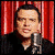 A person in a black shirt stands before red curtains with a microphone, while another scene shows the same person outdoors in a brown jacket against blue sky.