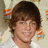 A person with brown hair and blue eyes wears a white shirt against a light background with orange and gray elements.
