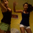 Two figures in dark tank tops and shorts pose with raised arms against a yellow background, one figure has long hair.