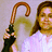 A pixelated image shows a person holding a curved brown cane with a dark green handle, wearing a white top against a light gray background.