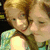 Two pixelated figures with light brown hair embrace closely, one wearing a light green top with a dark brown strap across the chest.