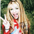Pixelated image of a person with long blonde hair wearing red and white clothing, making a peace sign gesture against a green background.