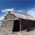 Pixelated image of a small stone building with a sloped roof under a blue sky with scattered clouds.
