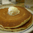 Stack of golden-brown pancakes with a pat of butter on top, displayed on a plate with blue and white striped pattern.