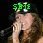 A person with long brown hair wearing a black cap with colorful dots sings into a microphone, with green text changing across frames.