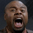 Pixelated close-up of a bald man with light brown skin, mouth open in an exaggerated shout against dark background.