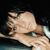 A pixelated close-up of a person's face with light skin, dark hair, and a hand near the cheek against a dark background.