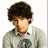 Pixelated image of a person with brown curly hair wearing a gray sweater over a white collared shirt, set against a blue background with pink text.