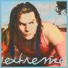 A person with long dark hair wearing a red sleeveless top, positioned against a blurred outdoor background with visible text "extreme" at the bottom.