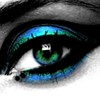 Close-up of a human eye with green and blue eyeshadow, black eyeliner, and a small white reflection in the pupil.